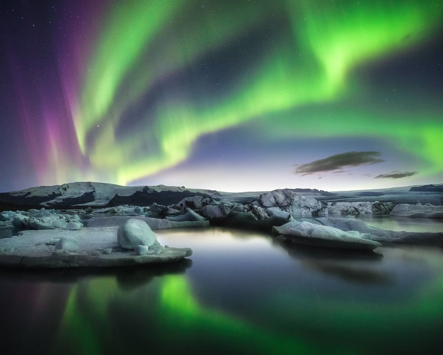 The Northern Lights (Aurora Borealis) illuminating the sky over a rugged Icelandic landscape.